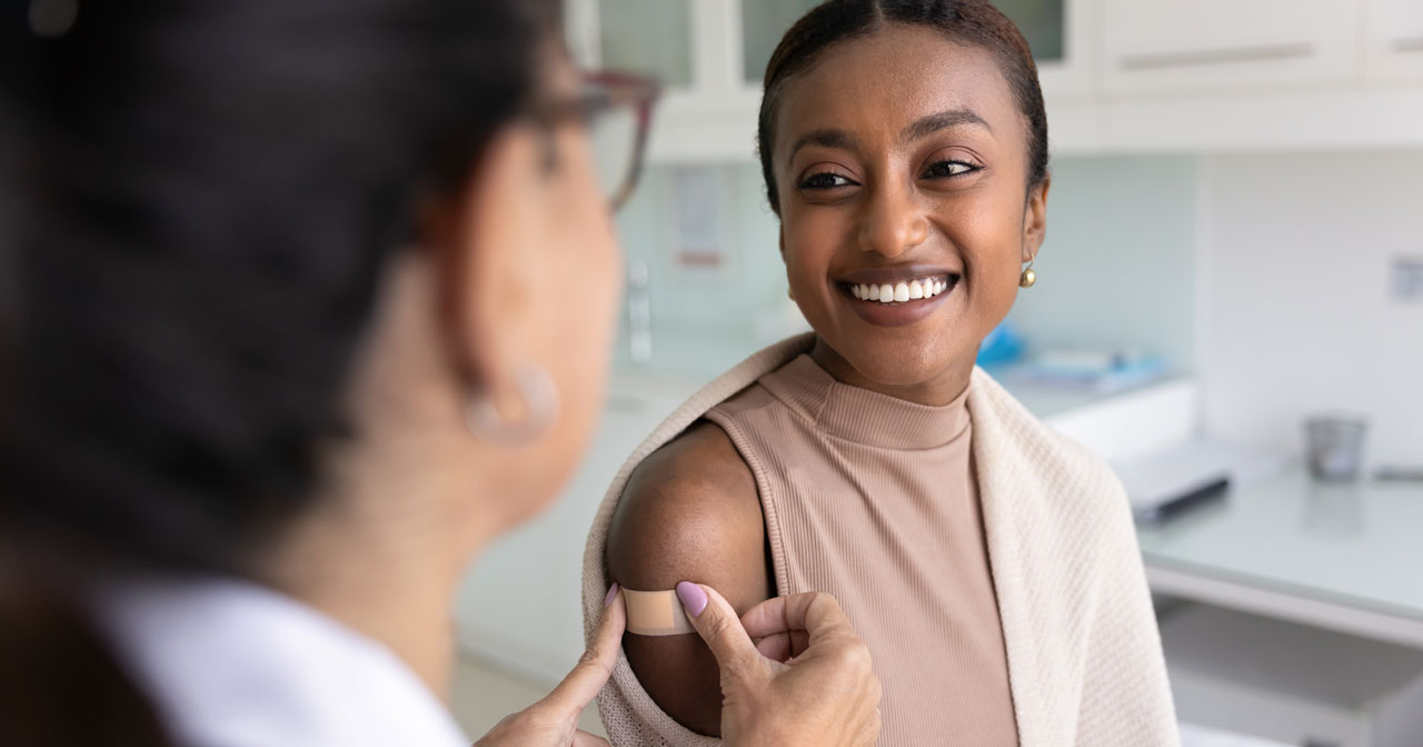 A healthcare provider places an adhesive bandage on the arm of a smiling woman