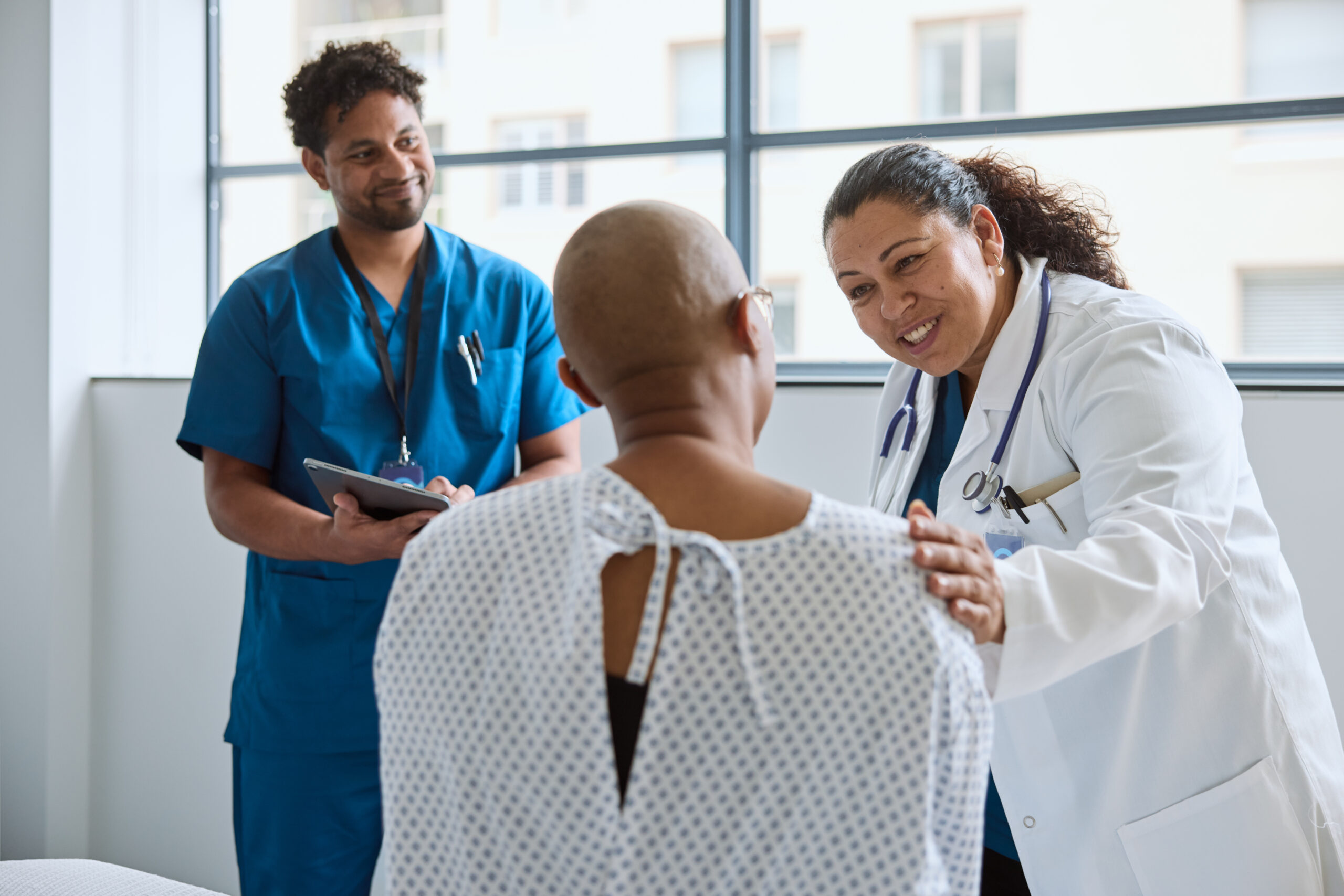 Photo of a patient in a gown with their back to the camera. The patient is speaking with a healthcare provider while another looks on. They're discussing choosing the right oncologist.
